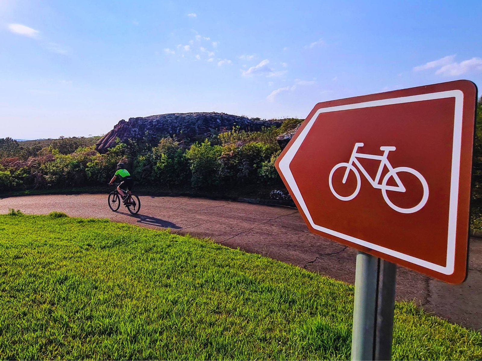 Ciclista pedala e visualiza o horizonte orientado pela placa de sinalização diretiva de cicloturismo.