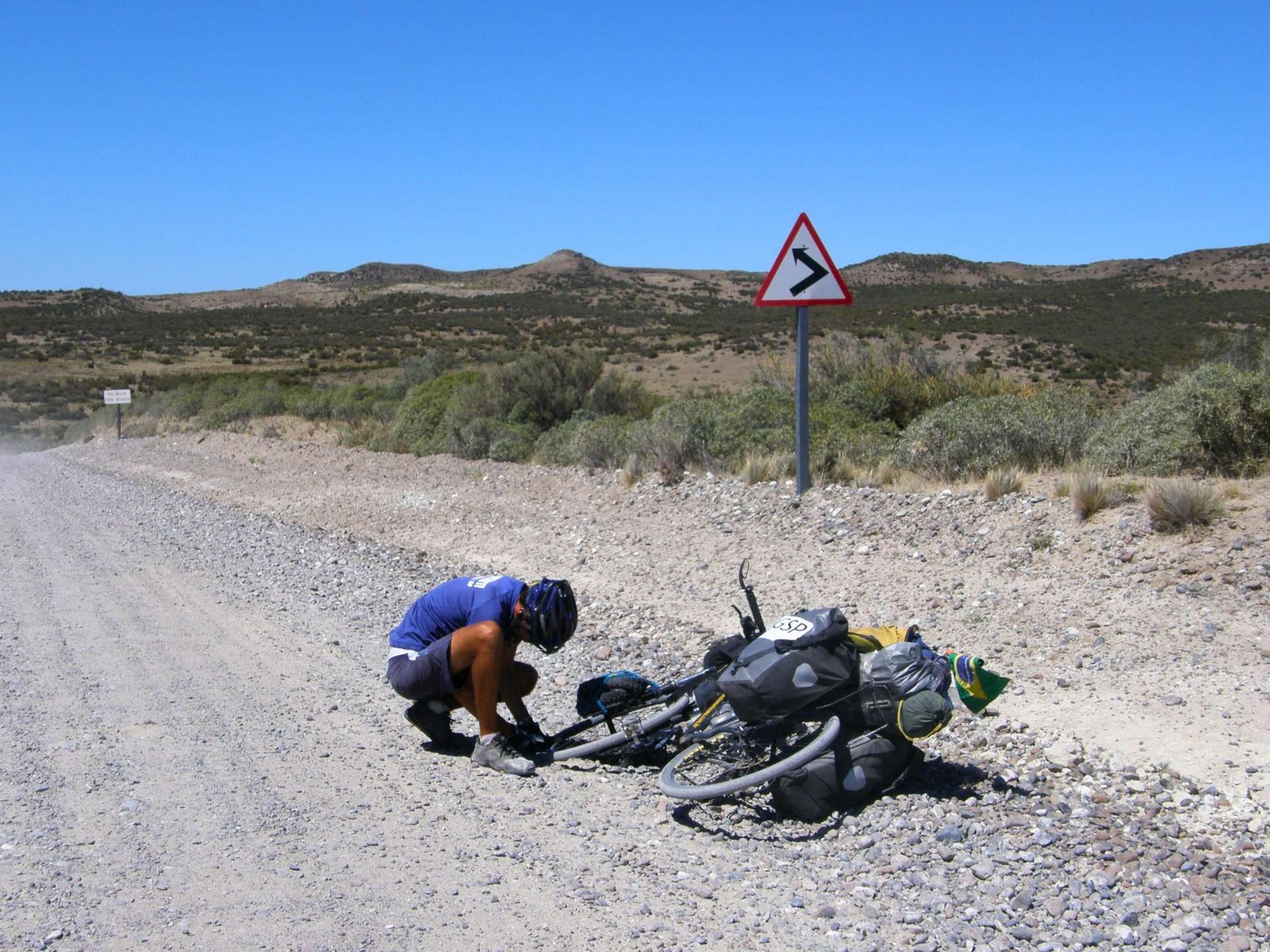 Ciclista conserta a sua bicicleta em trecho de estrada de chão.