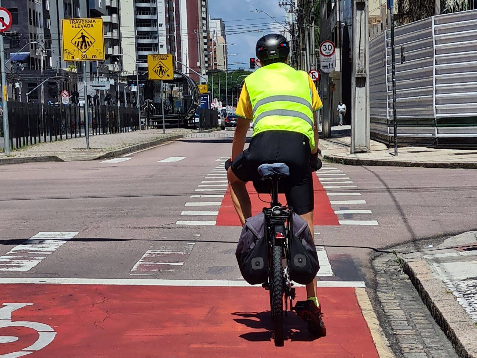 O ciclista observa a sinalização enquanto pedala na ciclofaixa com cicloestrutura.