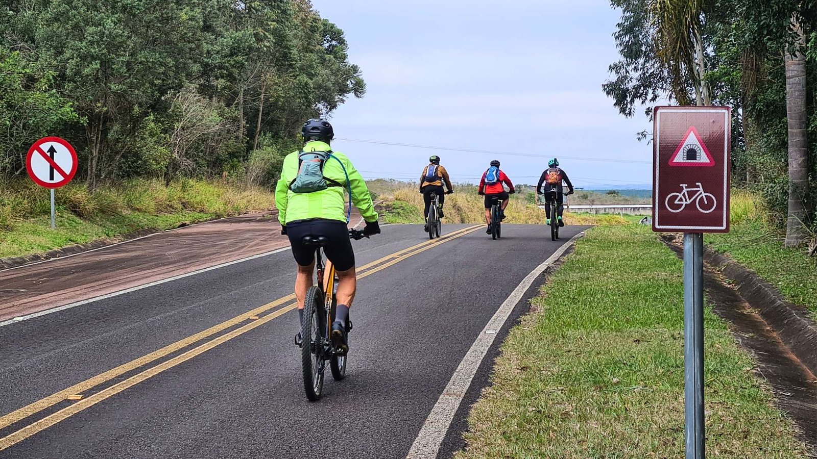 Ciclistas pedalam em grupo no asfalto com sinalização, redefinindo o conceito de cicloturismo autoguiado com mountain bike