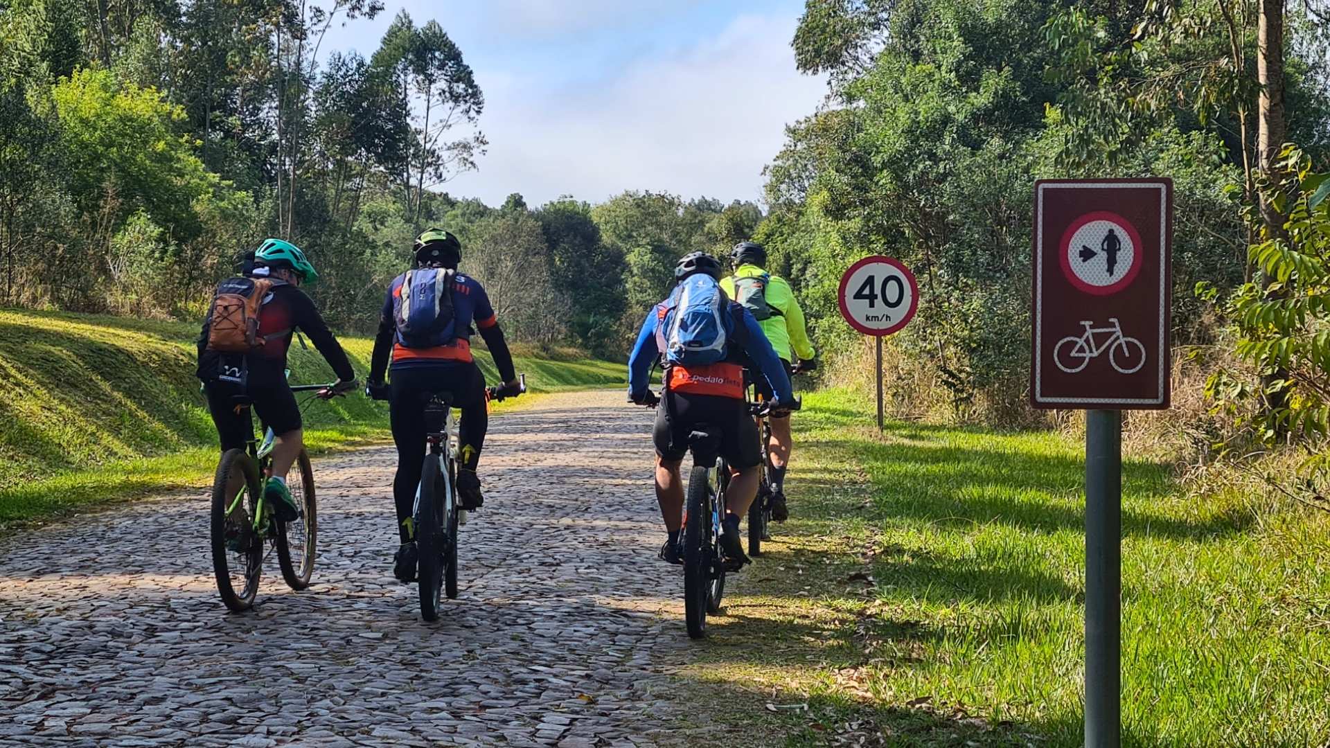 Ciclistas pedalam pela Rota dos Tropeiros com sinalização de cicloturismo autoguiado e contemplam a natureza e a cultura das comunidades locais.