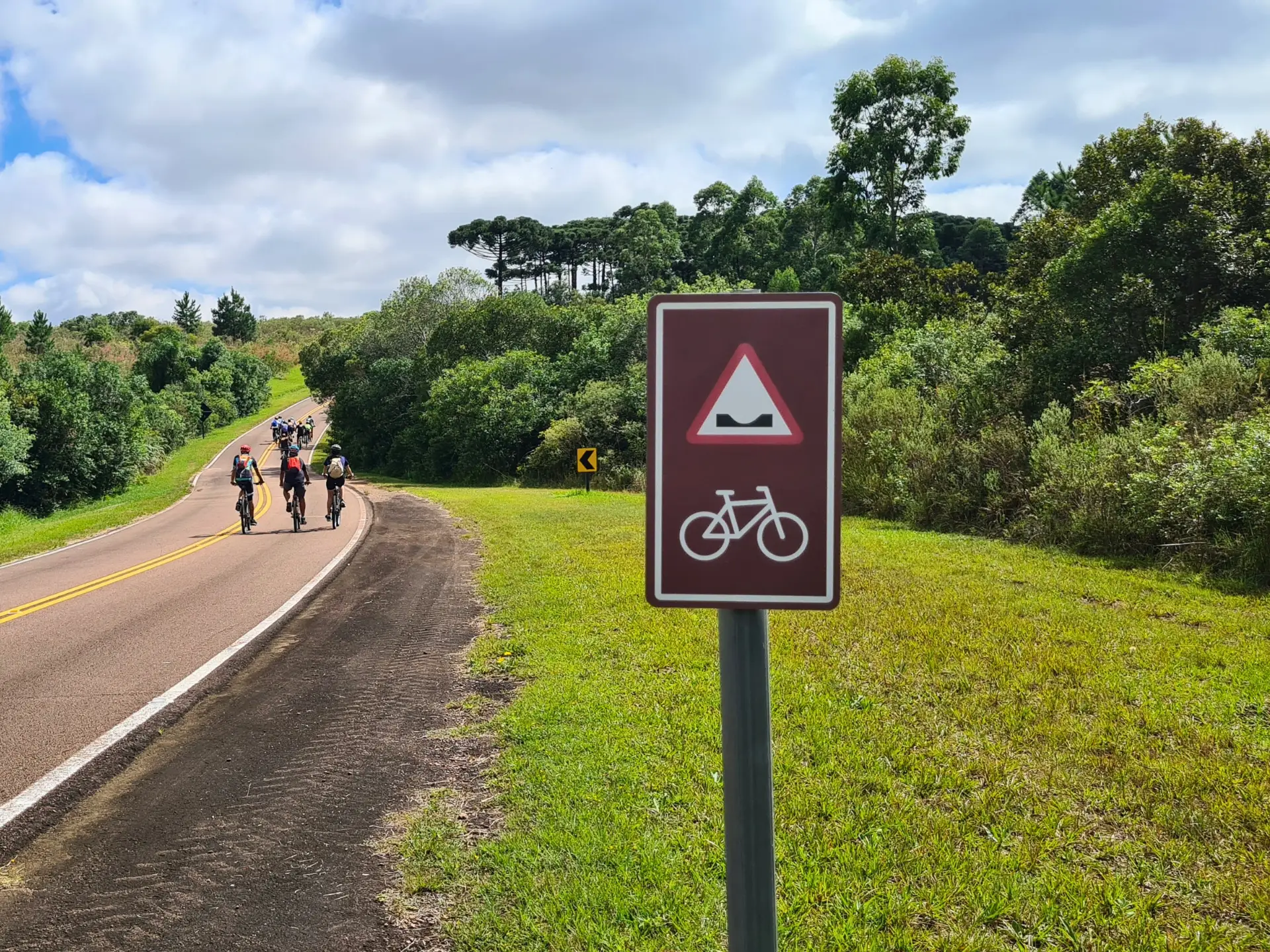Cicloturistas pedalando em estrada asfáltica sinalizada no Caminho das Tropas, Parque Vila Velha, ladeada por corredores ecológicos e vegetação nativa.